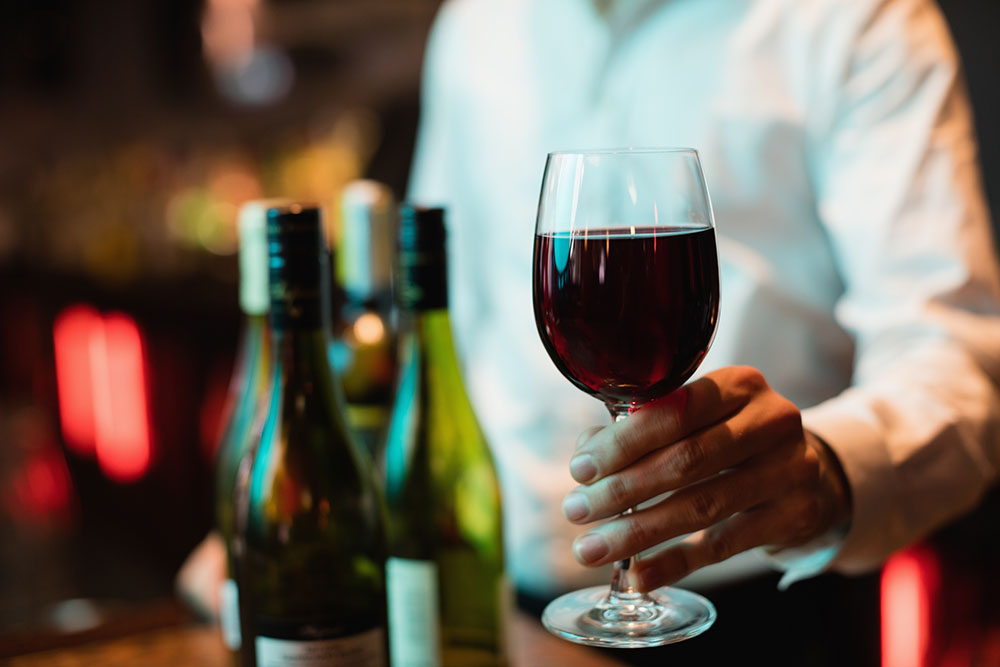 Mid section of bartender holding glass of red wine at bar counter